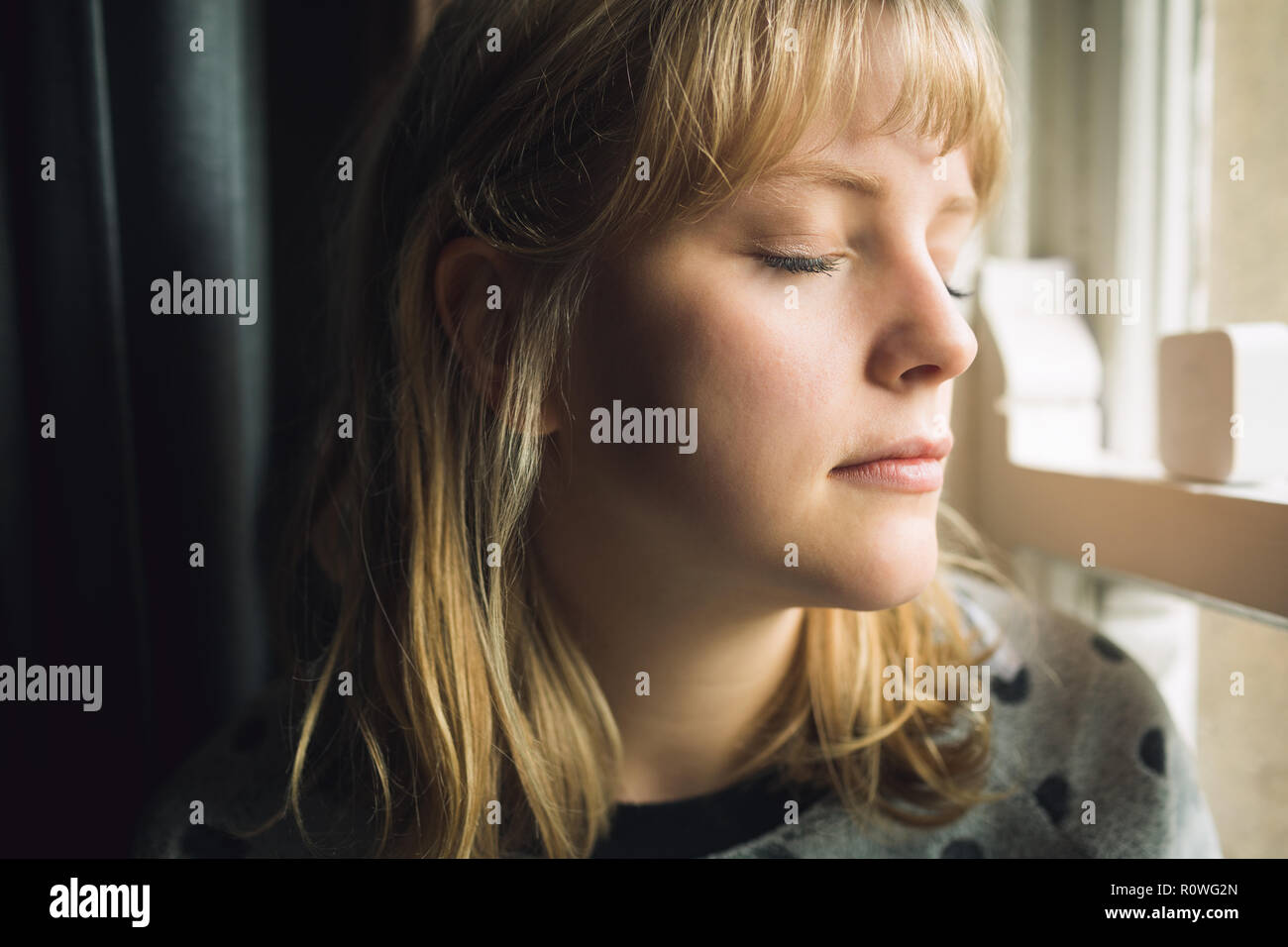 Woman with eyes closed sitting at window Stock Photo