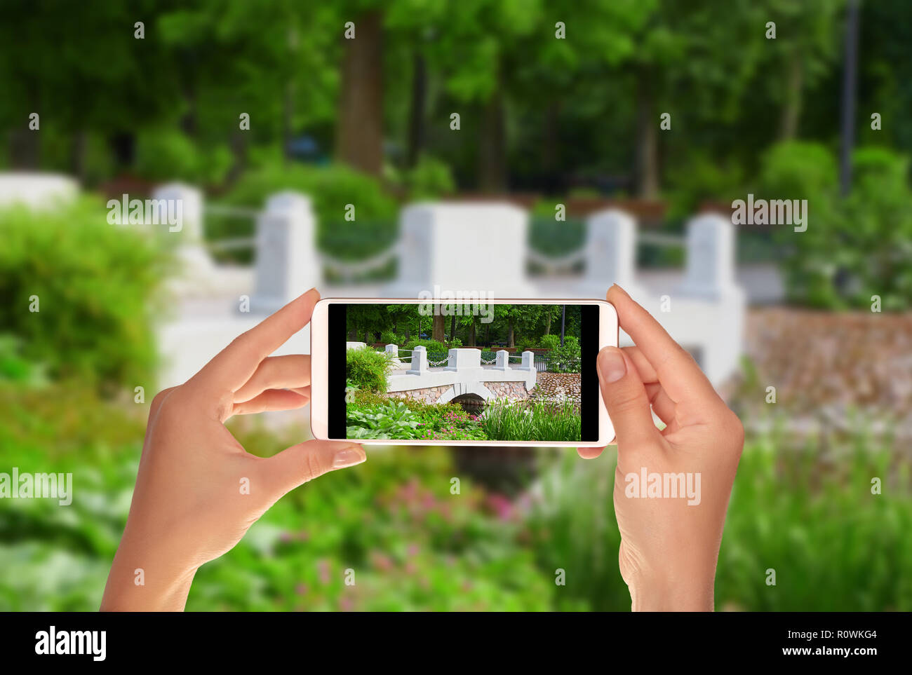A tourist is taking a photo of bridge over river in the Bernardine Garden in Vilnius on a mobile phone Stock Photo