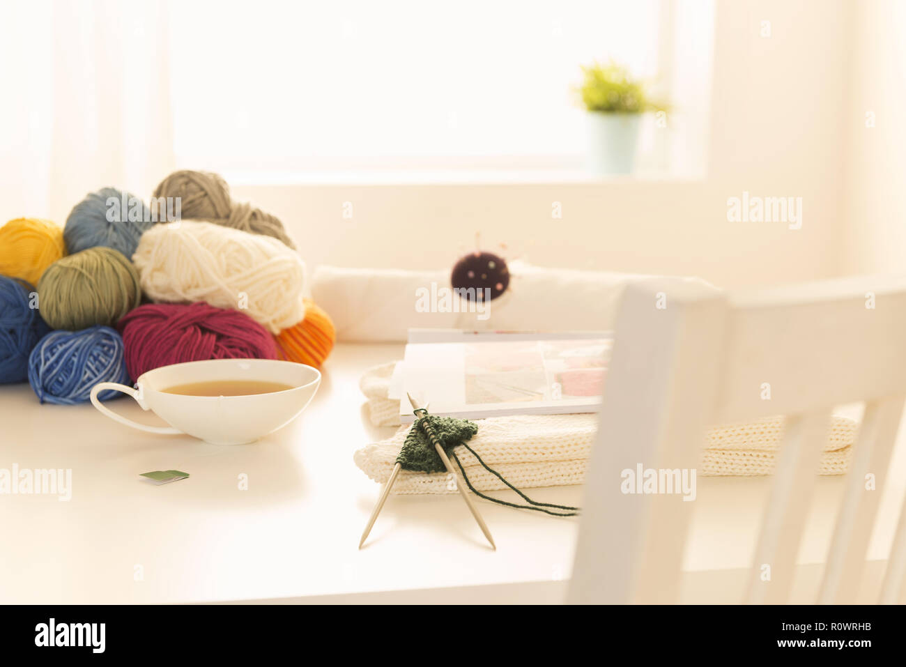 Wolle, Stricknadeln und Teetasse auf einem Tisch Stock Photo