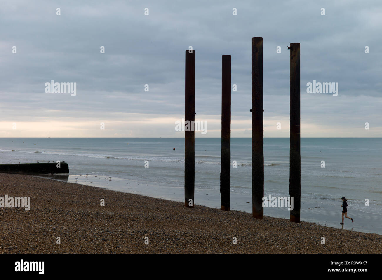 Jogger on beach running next to pillars from ruined West Pier, Brighton Stock Photo