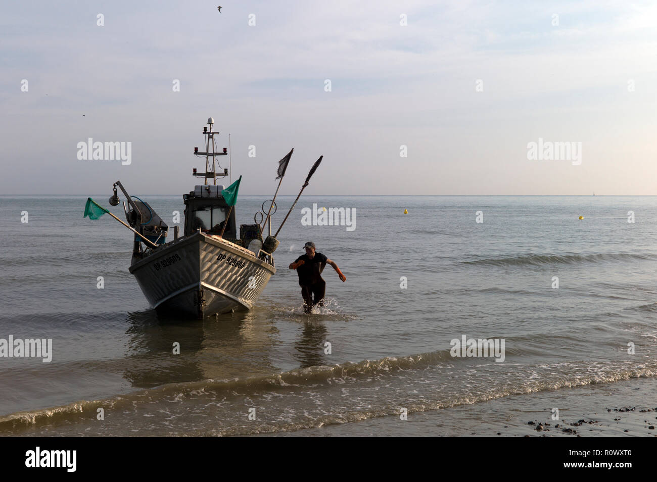 Fisherman running alongside his boat about to land on beach, Normandy,France Stock Photo