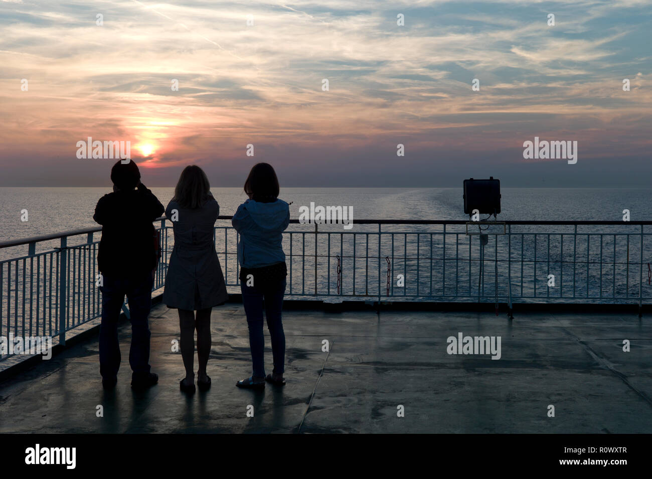 Three women photographing sunset from cross-channel ferry, silhouette Stock Photo