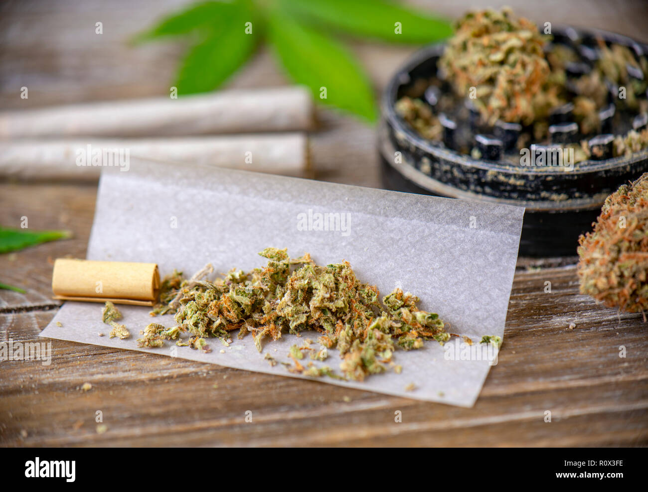 Cannabis joints with rolling paper and grinder over wood background
