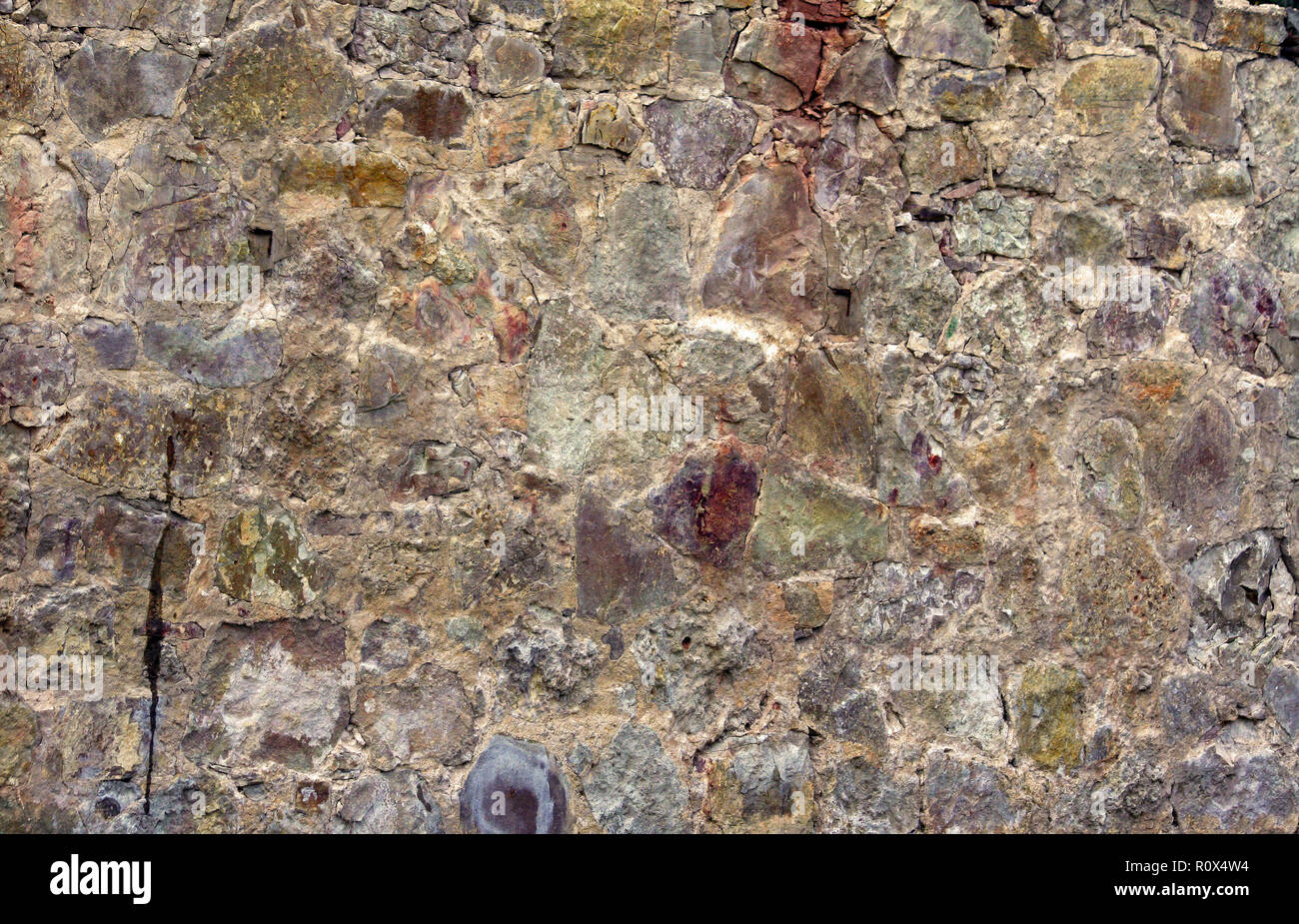 a piece of a flat stone wall, an old cracked surface consists of stones and rocks of various shades and structures, a variety of colors, old Stock Photo