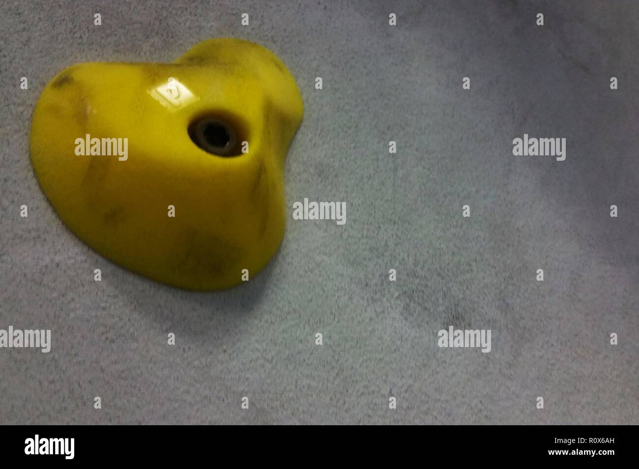 One yellow pincher rock climbing holds against a grey wall Stock Photo