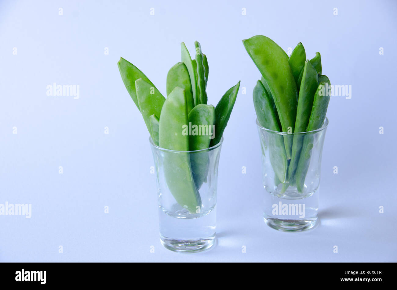 A bunch of snow peas standing up in a little glass on white background Stock Photo