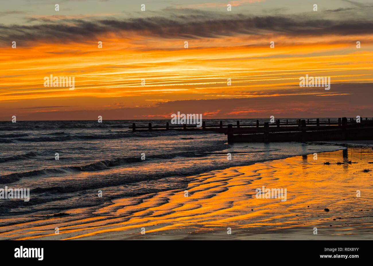 Evening sky after sunset with orange and red sky reflecting in sand ridges by the sea in West Sussex, UK. Stock Photo