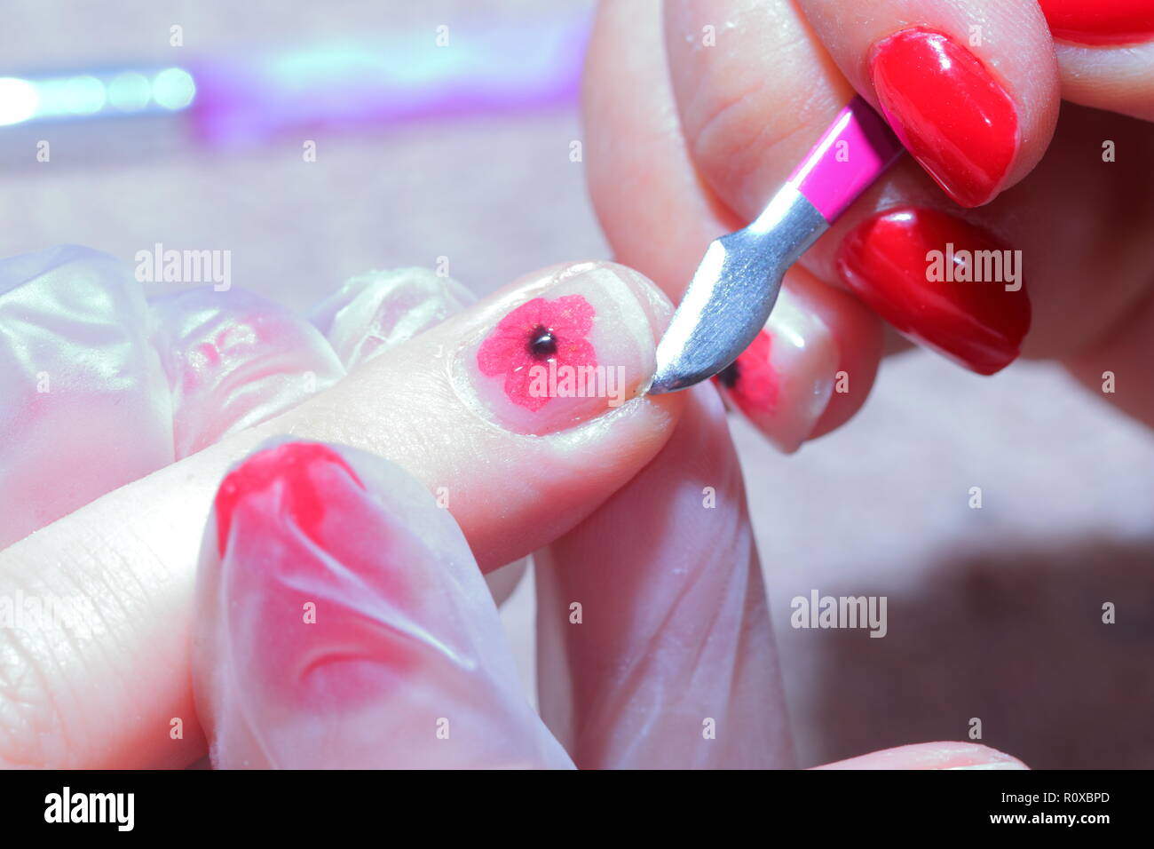 Nail technician applying a tiny poppy to a finger nail to mark remembrance day. Stock Photo