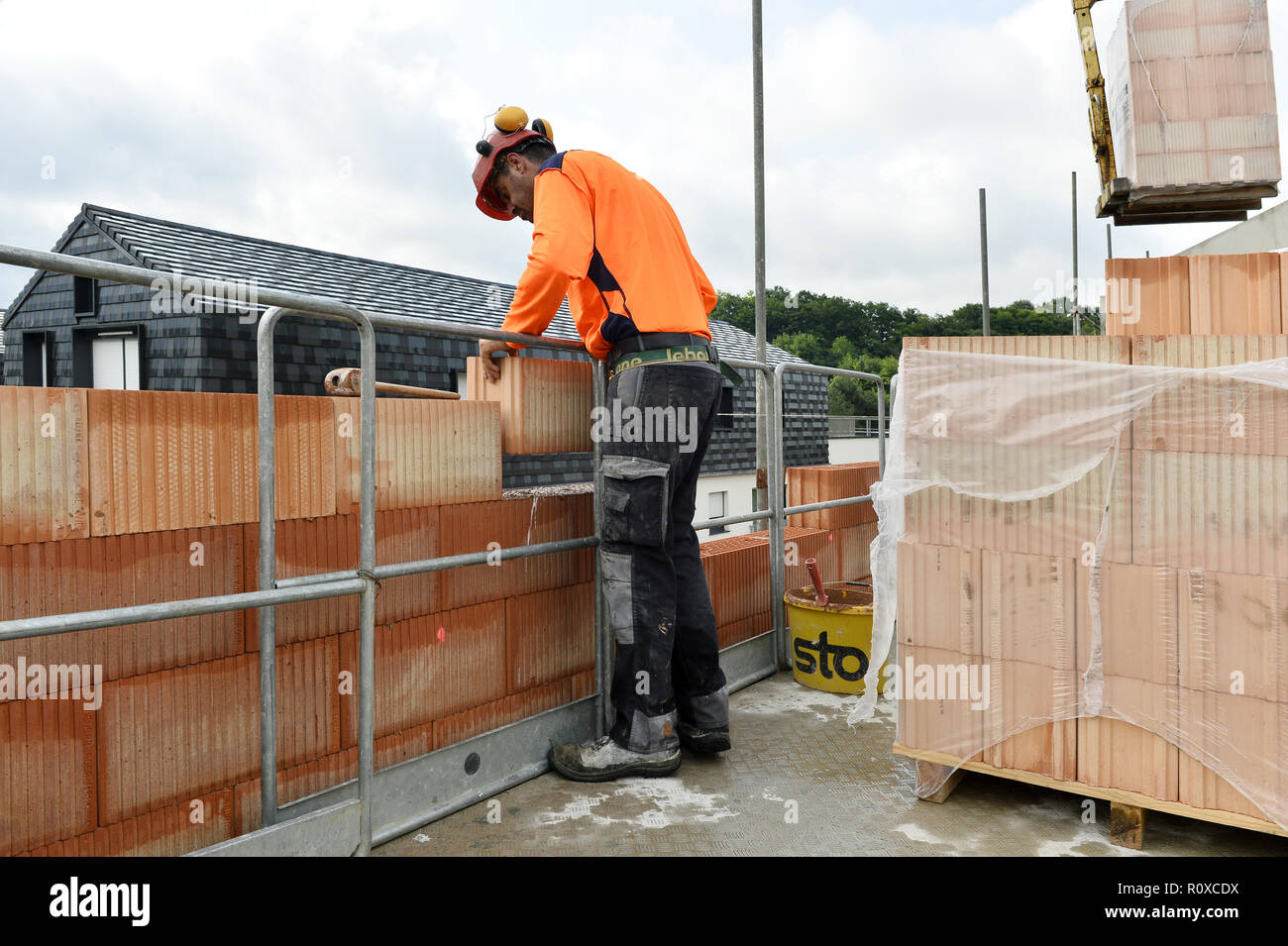 a construction worker building a wall with large orange-red clay blocks on an outdoor job site - France Stock Photo