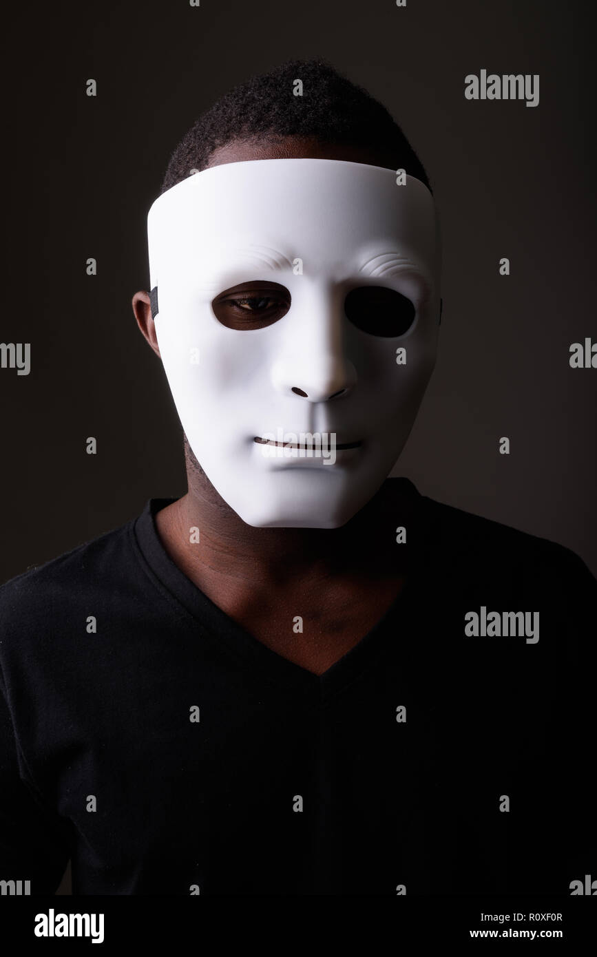 Portrait of young black African man in dark room wearing mask Stock Photo