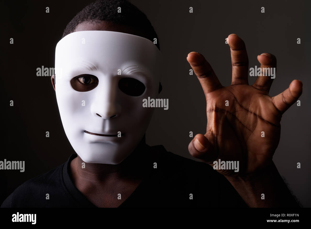 Studio shot of young black African man in dark room wearing mask Stock Photo
