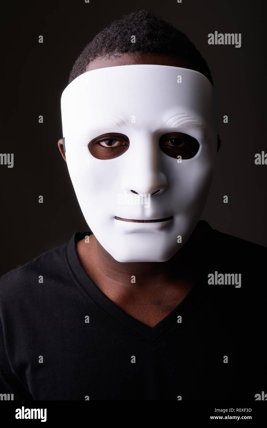 Portrait of young black African man in dark room wearing mask Stock Photo