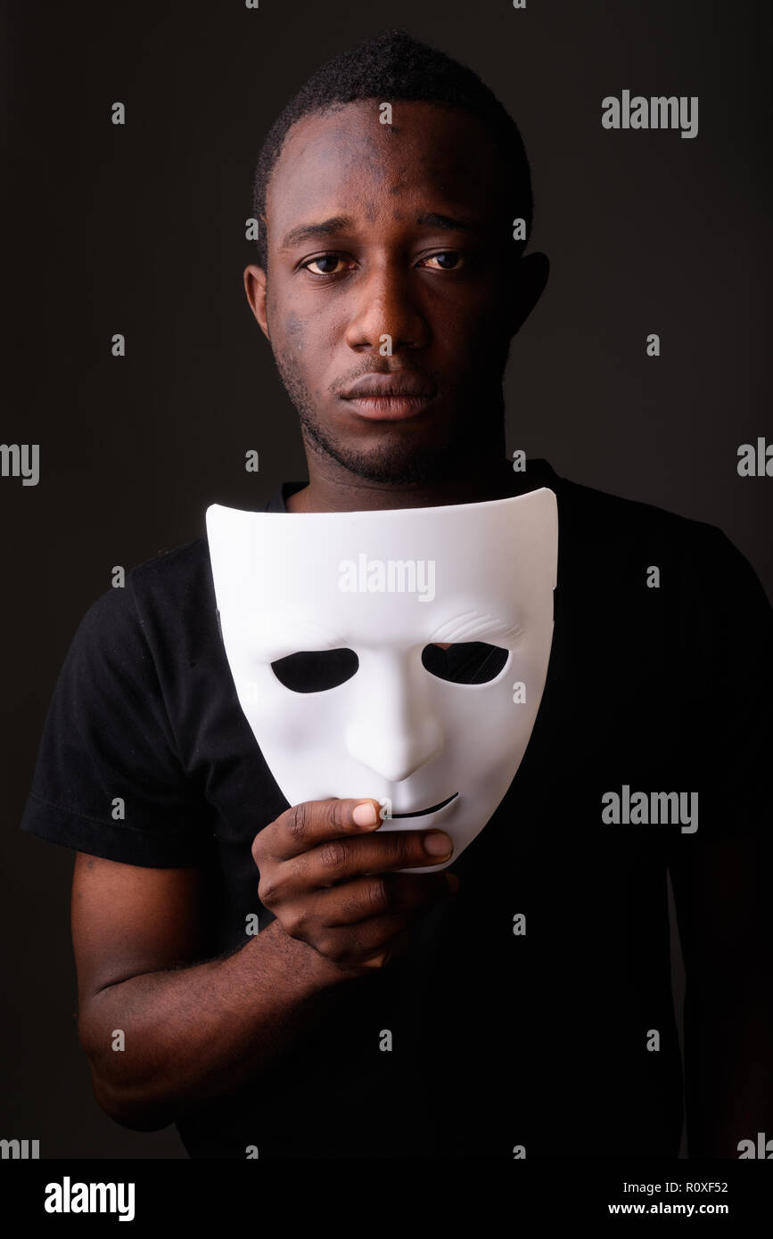 Portrait of young black African man in dark room holding mask Stock Photo