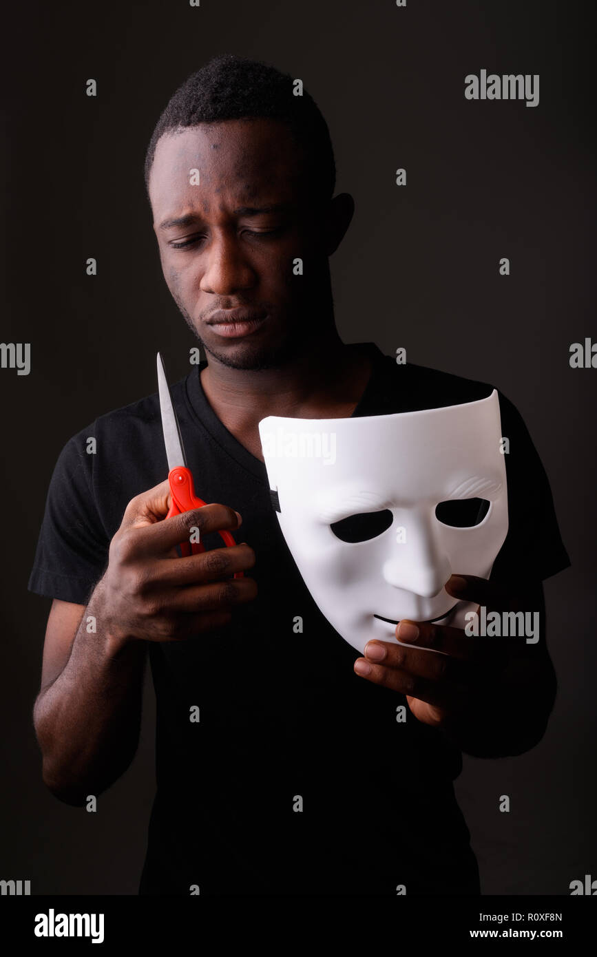 Studio shot of young black African man holding mask and scissors Stock Photo