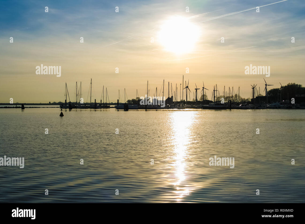 Lovely view of the sun setting behind the harbour leaving a silhouette of wind turbines and sailing boats with their mast on Fehmarn island in... Stock Photo