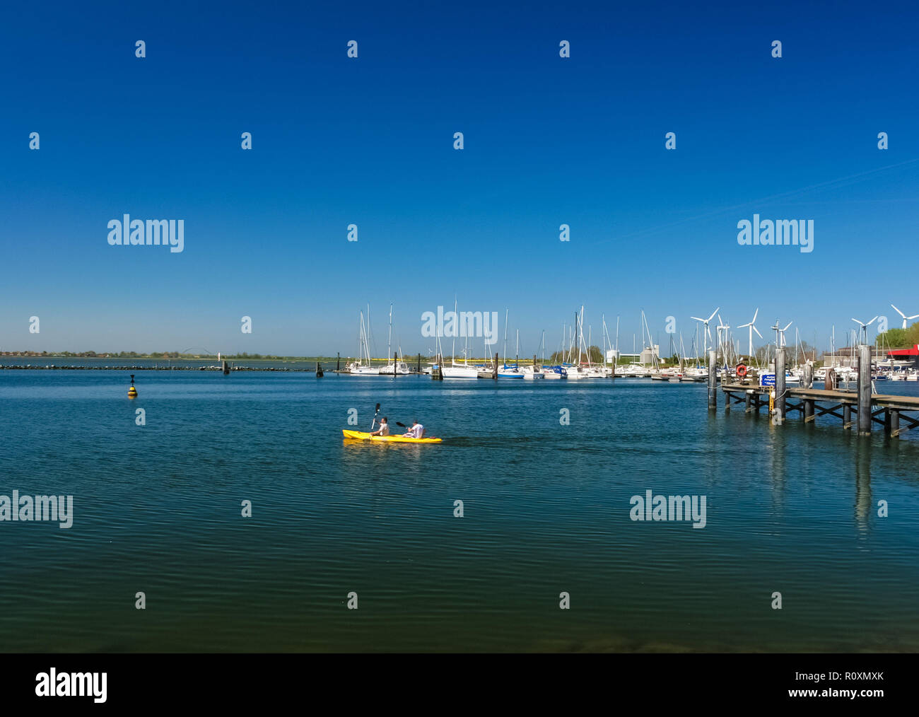 Picturesque view of two people canoeing on the sea with a bright yellow canoe at a jetty of Fehmarn island in Germany on a wonderful day with a nice... Stock Photo