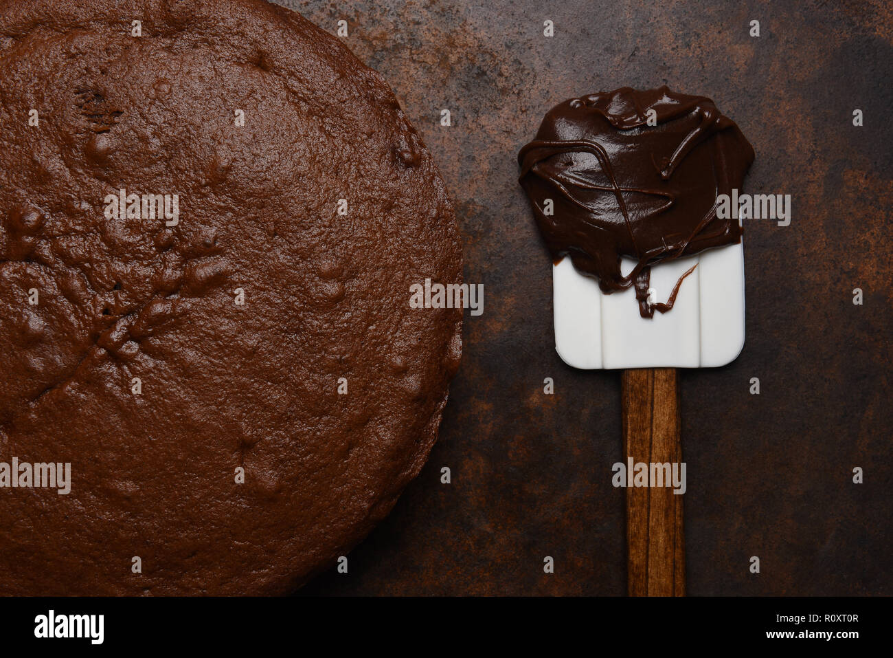Flat lay closeup of a unfrosted chocolate cake with a spatula and a glob of icing. Stock Photo