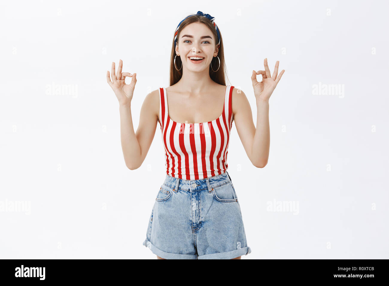 Friendly beautiful young woman in trendy pin-up striped top and shorts  showing okay gesture and