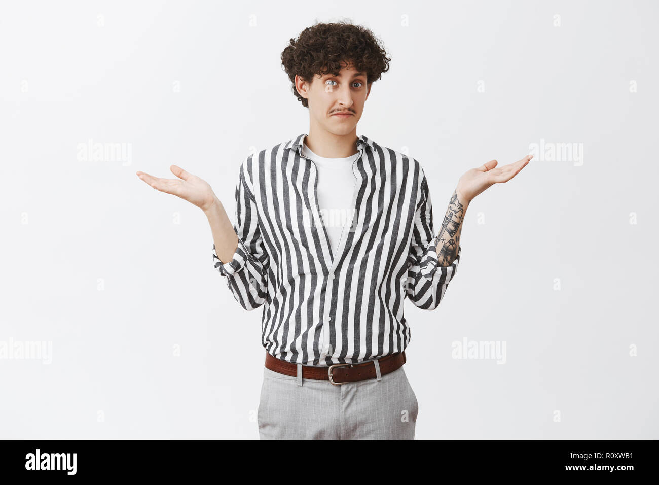 Waist-up shot of clueless good-looking and funny unaware guy with moustache and curly dark hair shrugging with spread palms having no idea feeling uncertain how to act or what answer Stock Photo