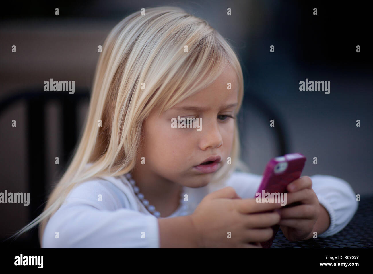 Young blond girl looking at pink cell phone with an intense look on her face. Stock Photo