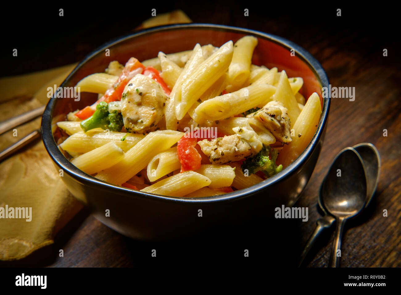 Grilled chicken alfredo penne primavera with dark moody lighting on rustic wooden kitchen table Stock Photo