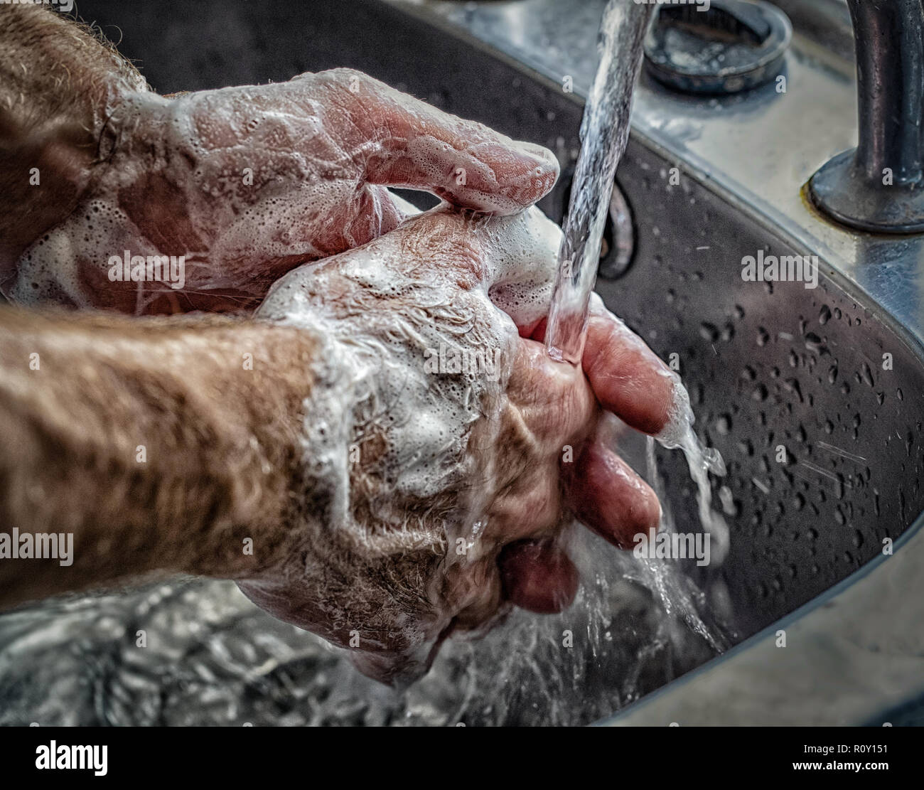 Man washing his hands with soapy water under a tap of running water in ...