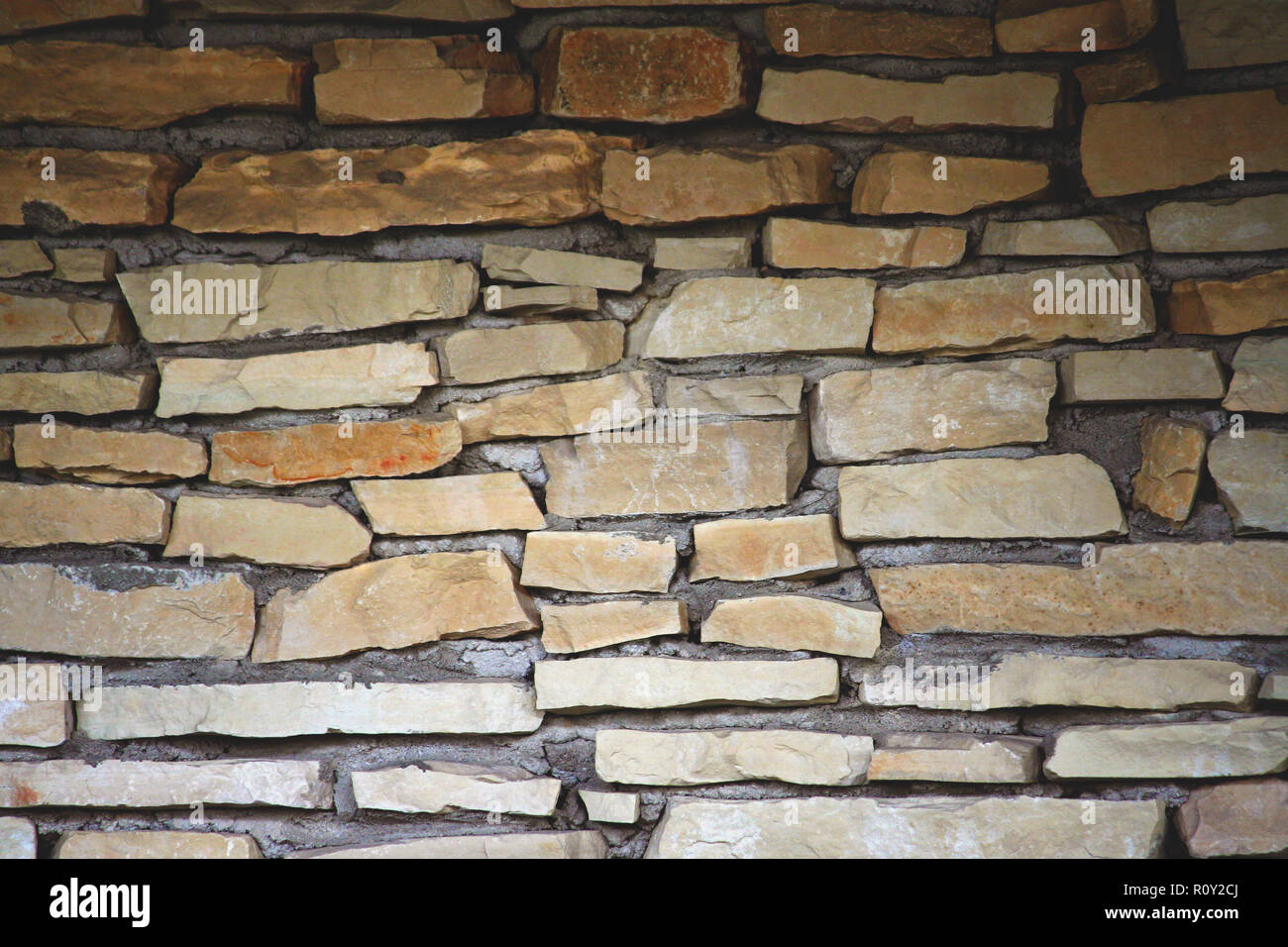 part of the wall is made up of individual pieces of stones in cement, the dark upper part is gradually lighter down, yellow and brown shades, Stock Photo