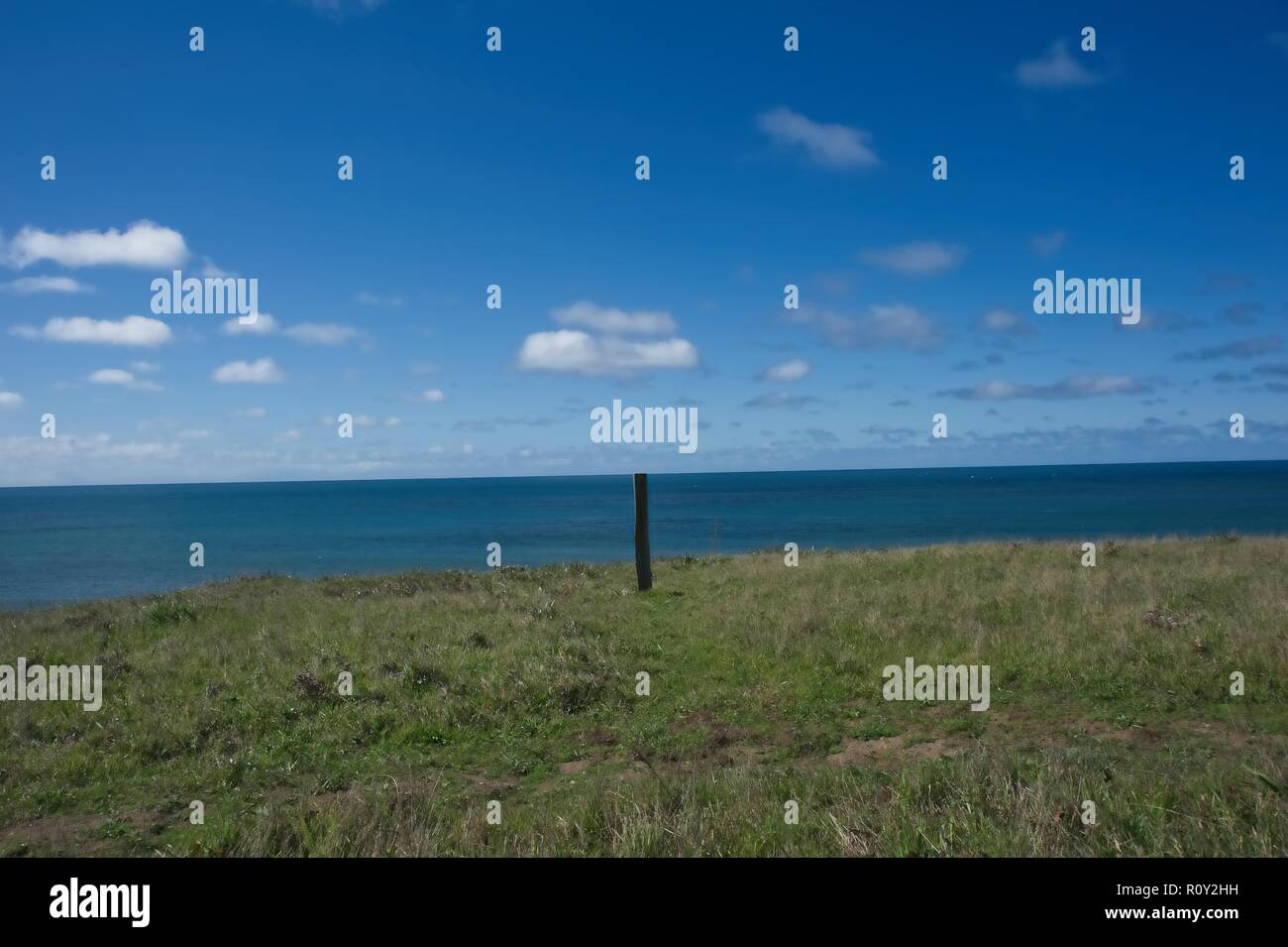 Pacific Ocean view with a post in the view from the grassy overlook on a clear day with some puffy clouds Stock Photo