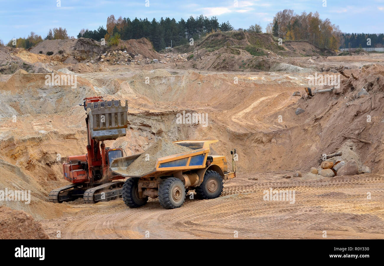 Large quarry dump truck. The excavator loading of a stone in the dump