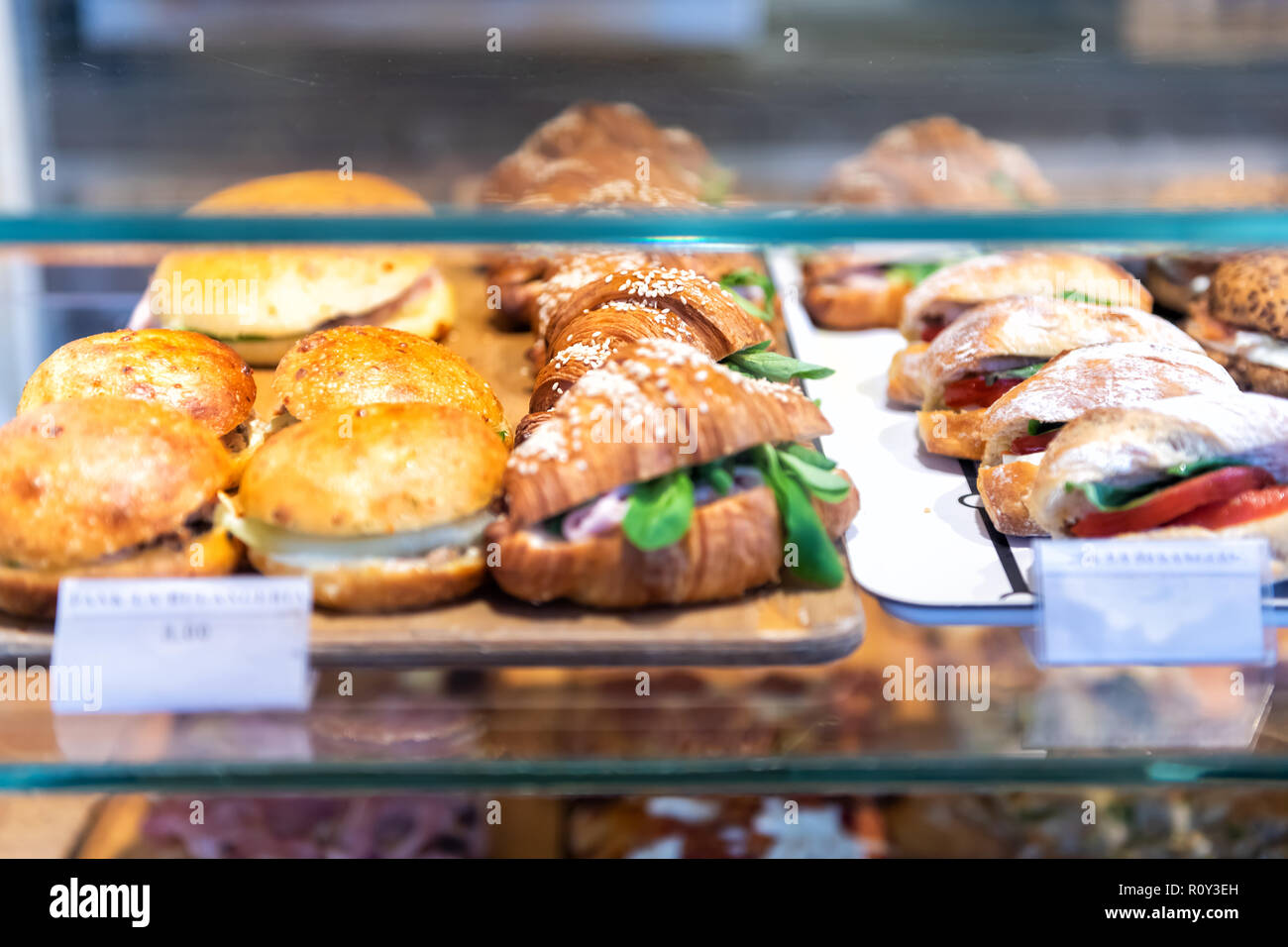 Display of store, shop selling Italian panini sandwiches with deli bologna meat, ricotta cheese, tomatoes, green spinach, buns, croissants on tray, pl Stock Photo