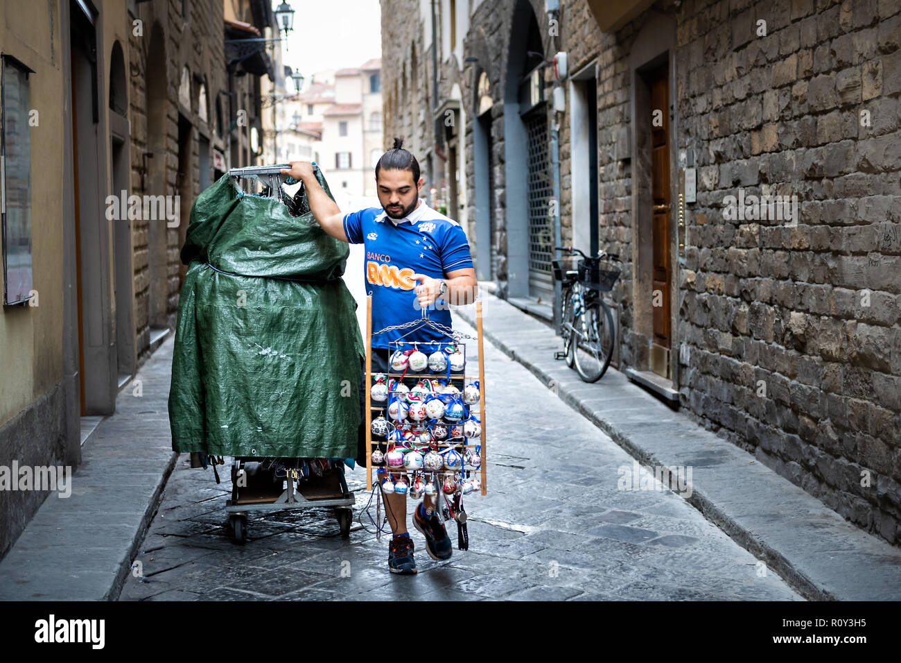 Florence, Italy - August 31, 2018: Young Italian man, street vendor, seller at Firenze Mercato di San Lorenzo, walking in narrow alley, holding souven Stock Photo