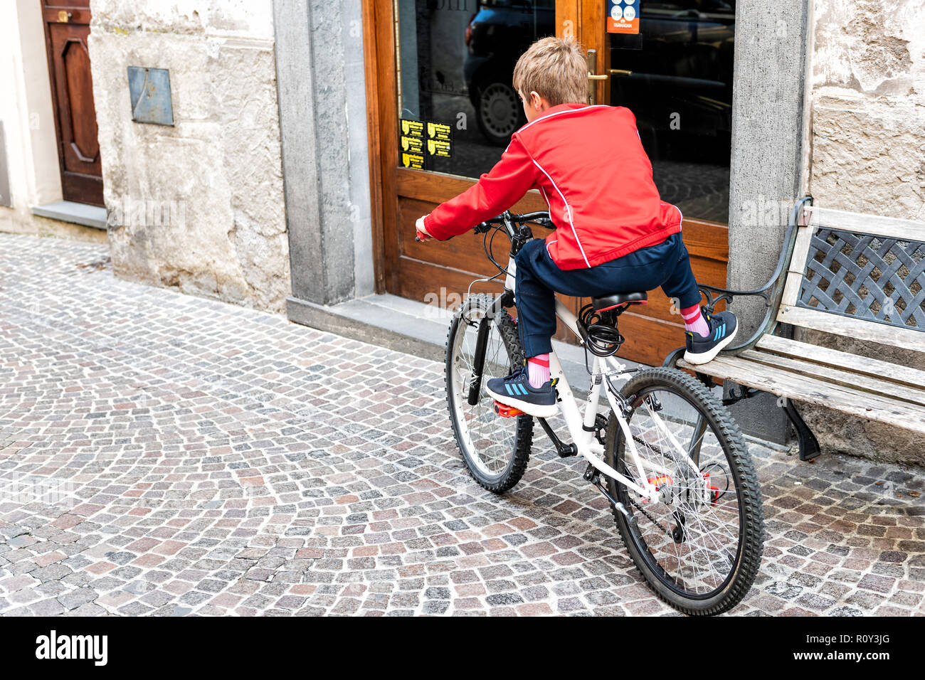 Orvieto, Italy - September 3, 2018: Young teenager, boy sitting on standing bicycle with one leg on bench, balancing, keeping balance in Italian small Stock Photo