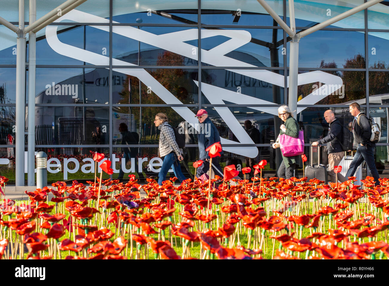 London Southend Airport, Essex, UK. To mark the centenary of the end of World War One a commemorative garden has been opened outside the terminal at London Southend Airport consisting of 2000 red ceramic poppies made by hundreds of children from 25 Southend schools. The airport served as RAF Rochford during both World Wars. Holiday passengers head towards departures passing the poppies Stock Photo