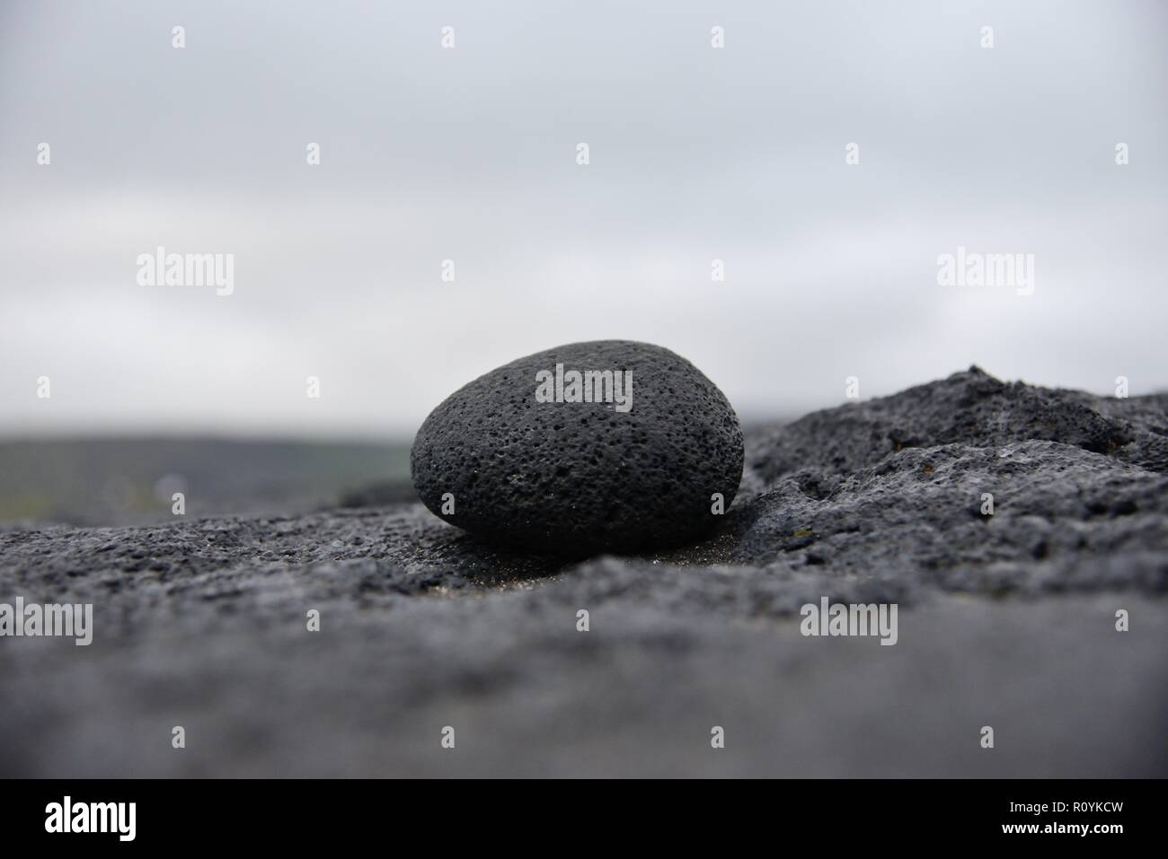 Round lava stone on black volcanic rock under a cloudy sky Stock Photo ...