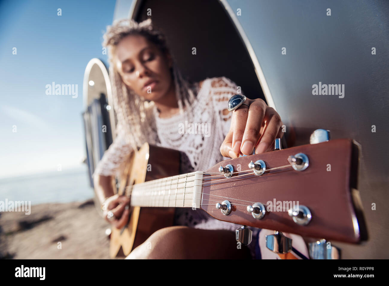Close up of woman with dreadlocks tuning the guitar sitting in trailer Stock Photo