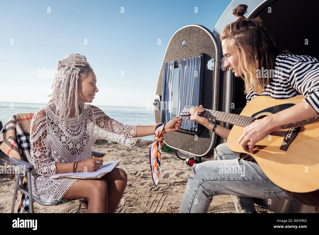 Girlfriend with white dreadlocks tuning the guitar for her boyfriend Stock Photo