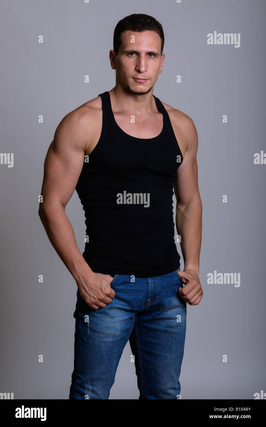 Studio shot of young muscular Persian man standing against gray  Stock Photo