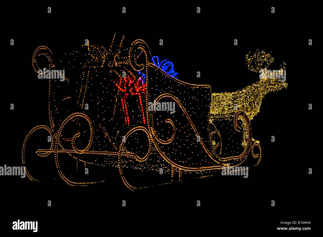 Christmas ilumination of a reindeer with sleigh carrying gifts in a garden outside Stock Photo