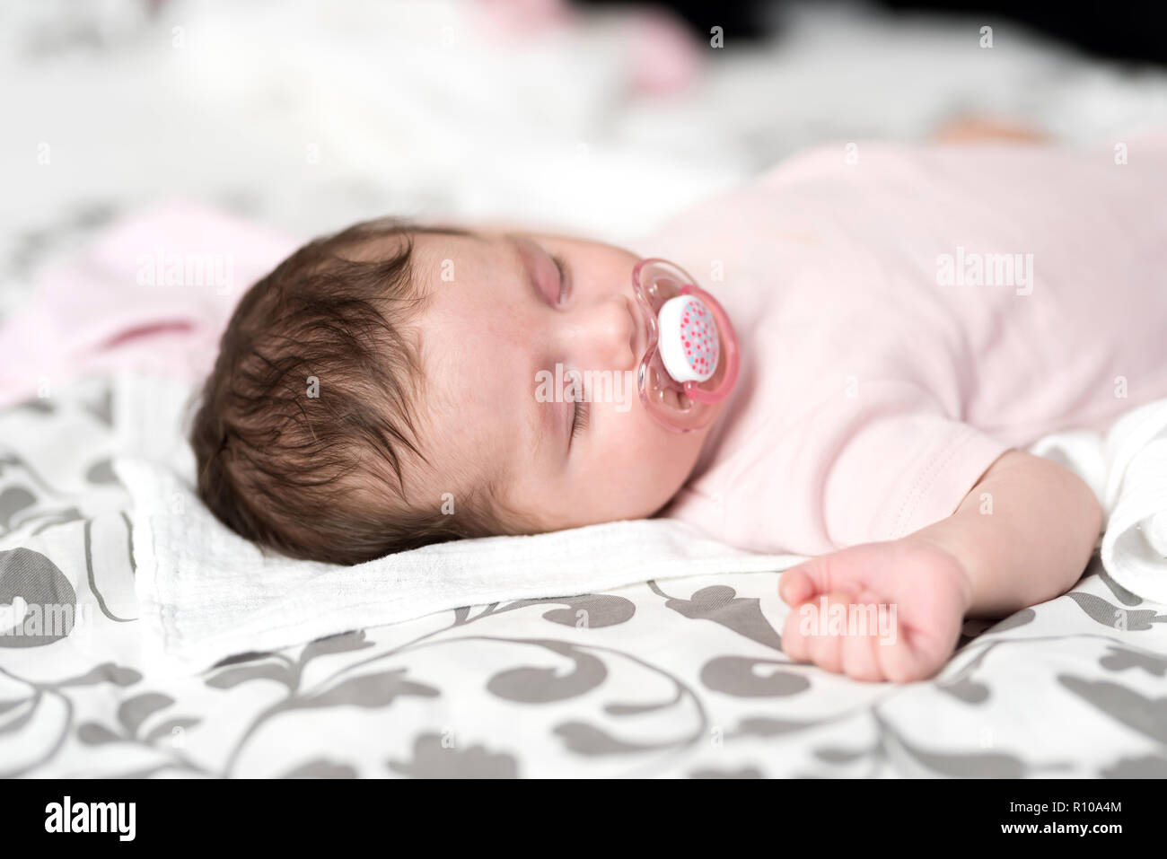 Closeup photo of a baby girl lying on a bed and sleeping with a dummy