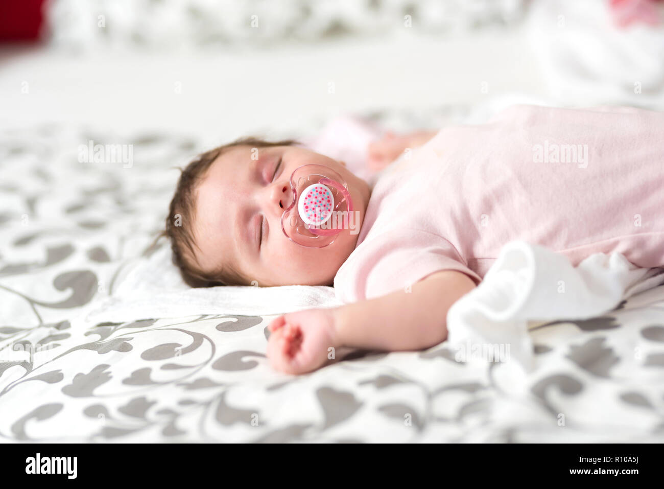 Closeup photo of a baby girl lying on a bed and sleeping with a dummy