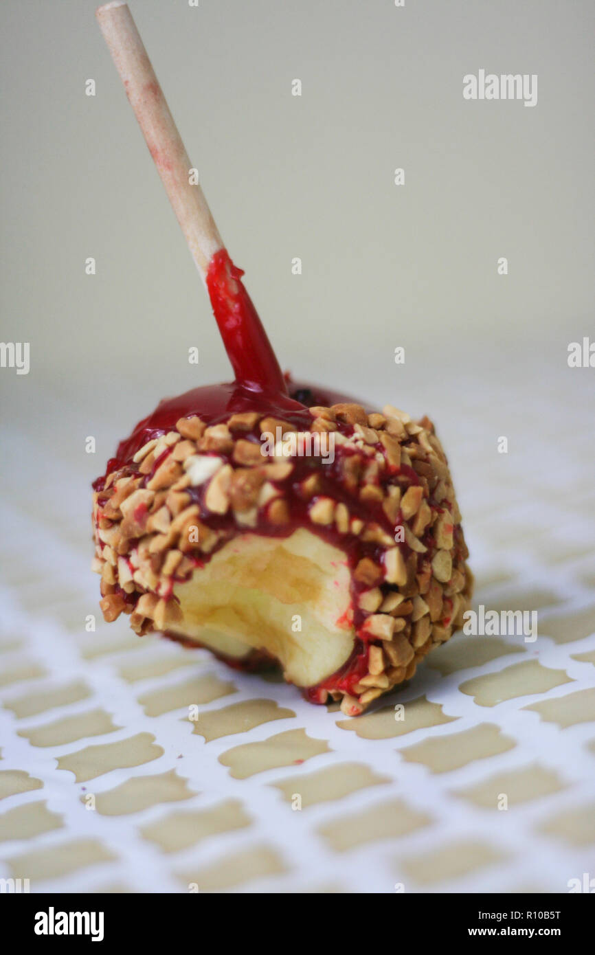 Red candy apple covered in peanuts with a bite taken out on a vintage pattern background. Stock Photo