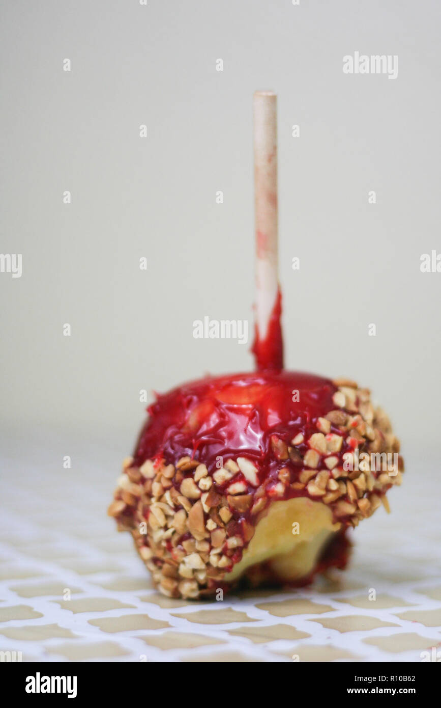 Red candy apple covered in peanuts with a bite taken out on a vintage pattern background. Stock Photo