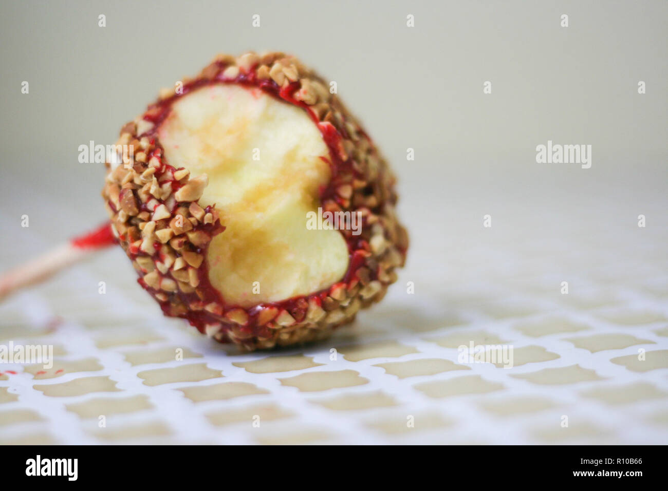Red candy apple covered in peanuts with a bite taken out on a vintage pattern background. Stock Photo