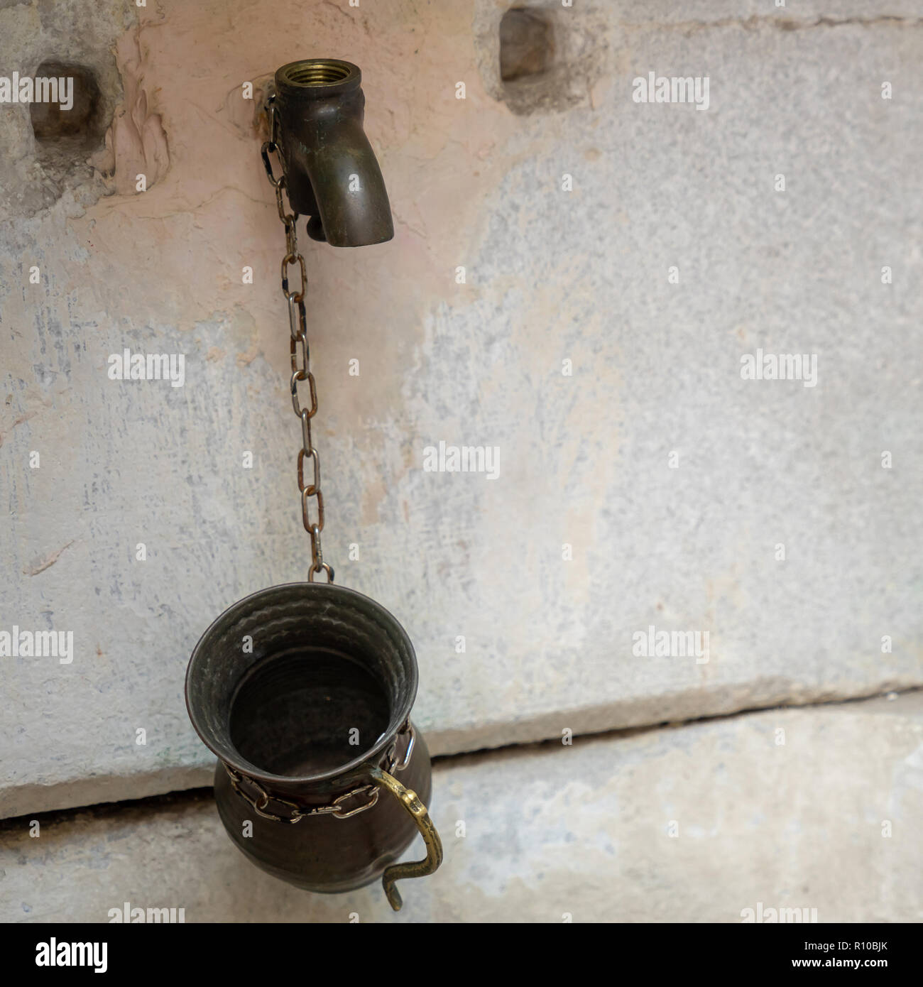 Historical bronze mug on a chain near a tap to quench the thirst of