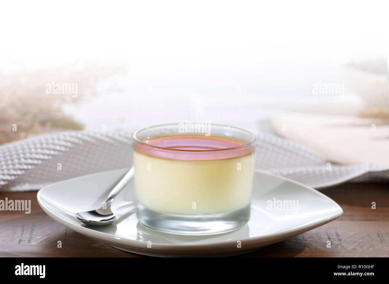 Close up of glass pudding creme caramel on plate with spoon, white tablecloth Stock Photo