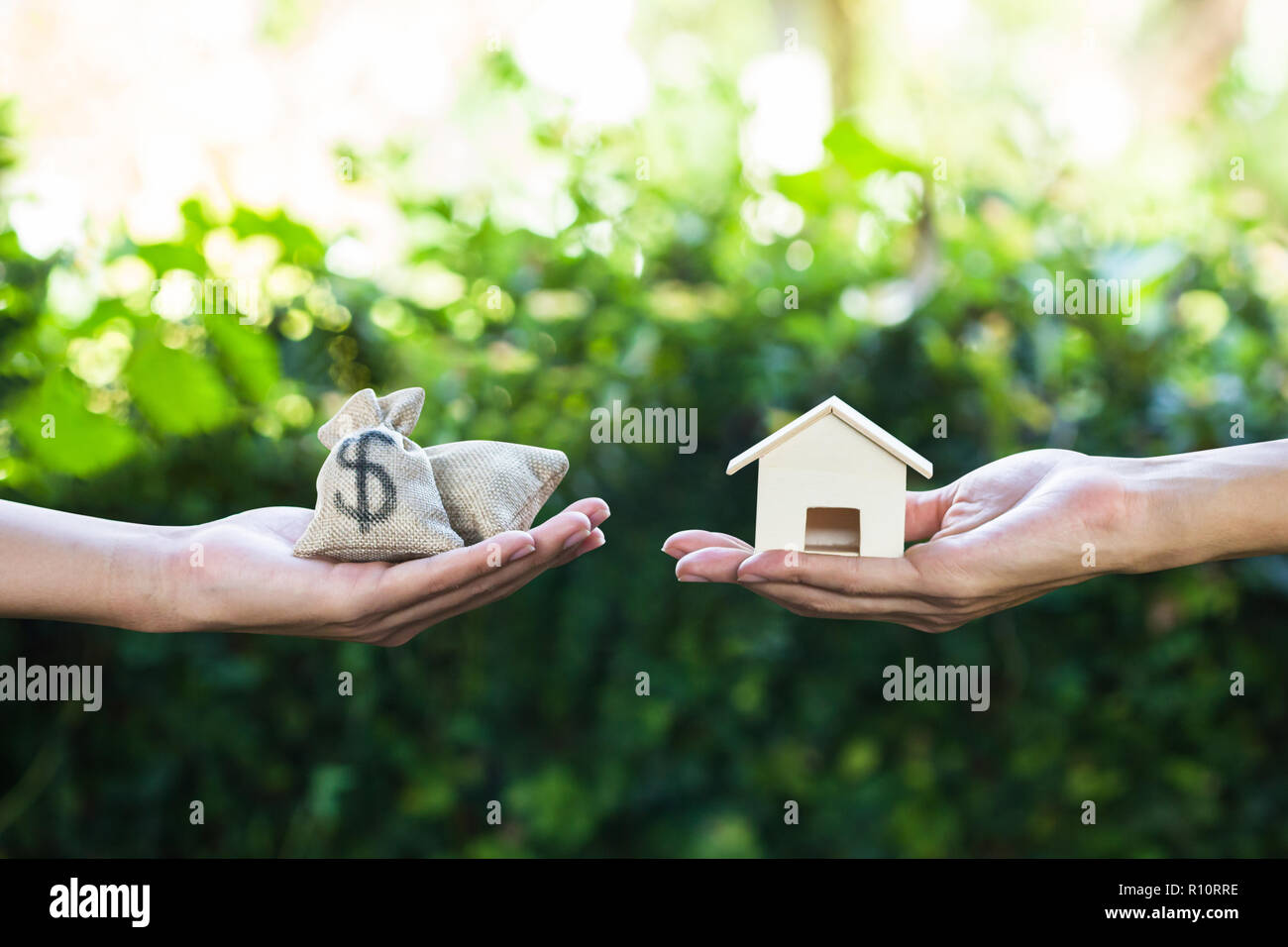 Home loan, lending, mortgage, transforming assets into cash concept : Hand holding home model change to money with green nature as background. Concept Stock Photo