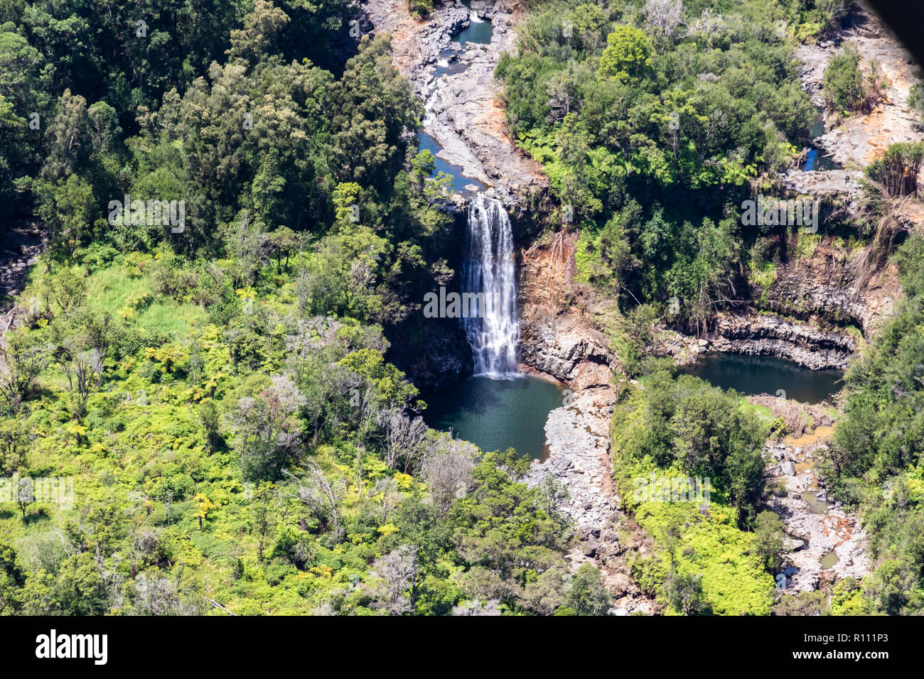 Aerial view of waterfall near Hilo, Hawaii. Water flows over rock into pool below; Rainforest crowds both banks. Second pool is nearby. Stock Photo