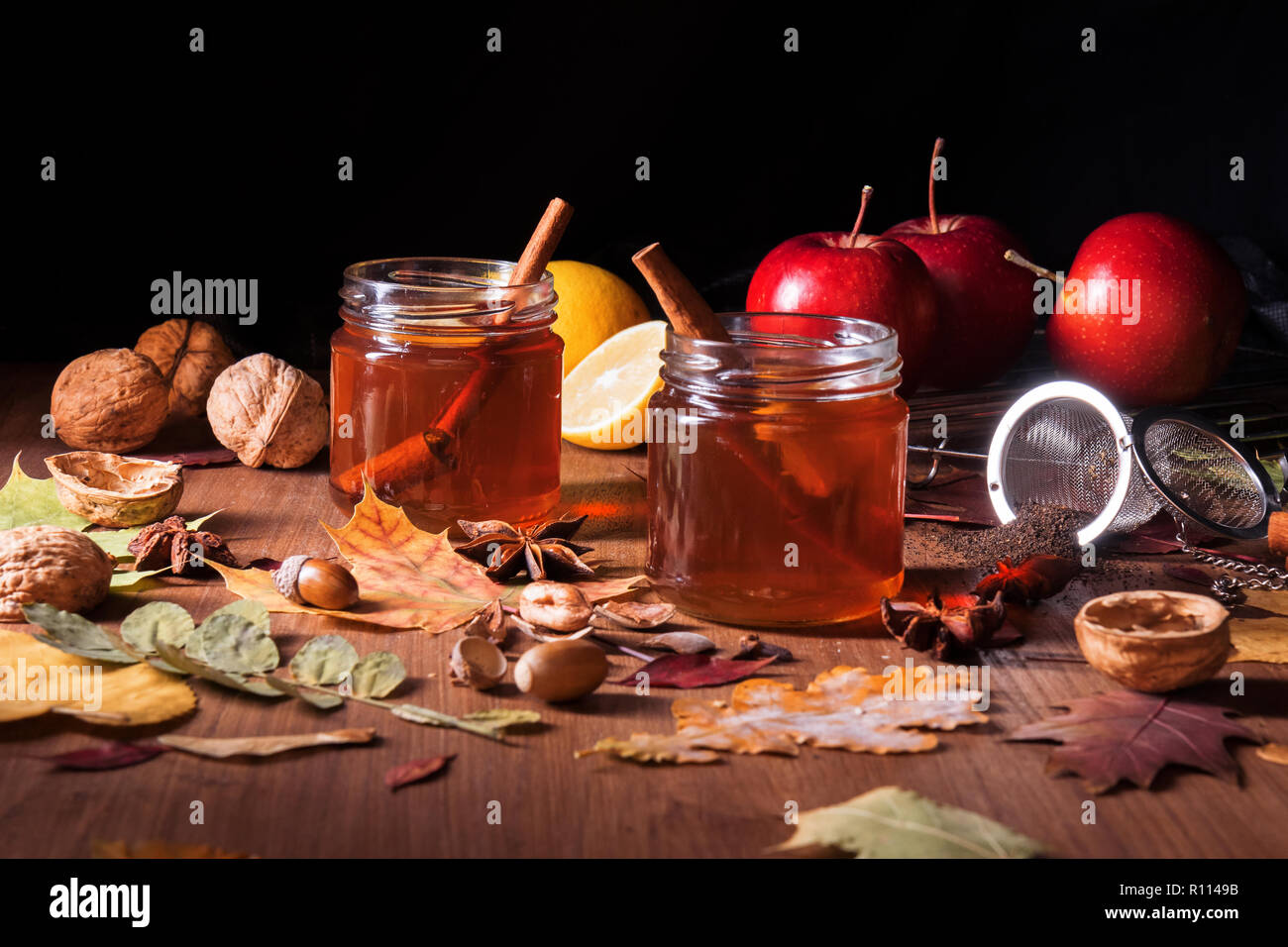 Dark wooden table with 2 glasses of tea with fall, autumn decoration and dark, black background. Colorful leaves, lemon, cinnamon, walnuts, apples, te Stock Photo