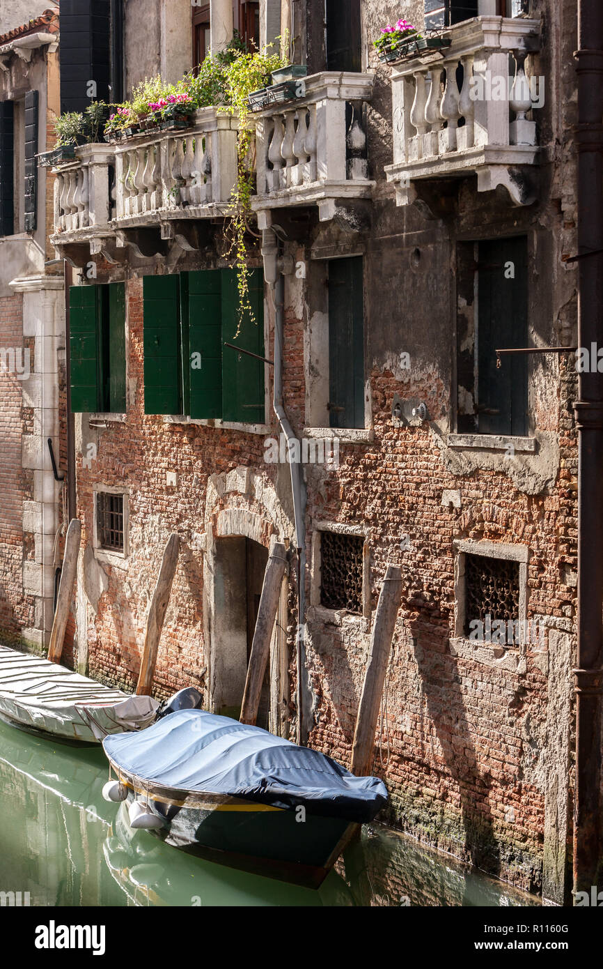 Old brick and painted buildings with balconies and doorways with covered  gondala boats on the canals of Venice Italy Stock Photo