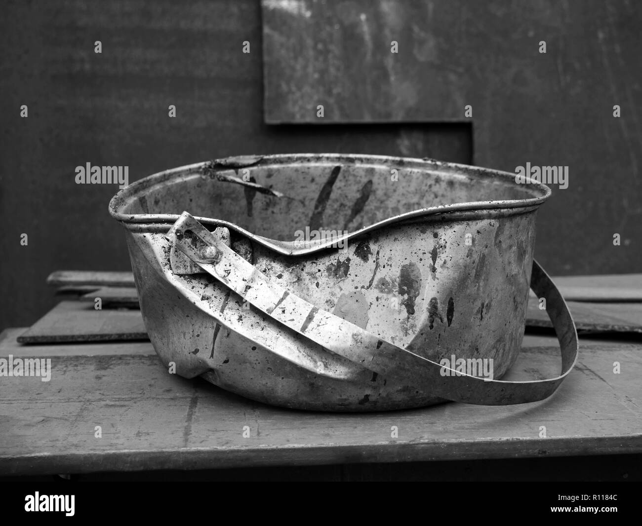 Dented metal bucket discarded, used for paints and liquids in a working boatyard. Stock Photo